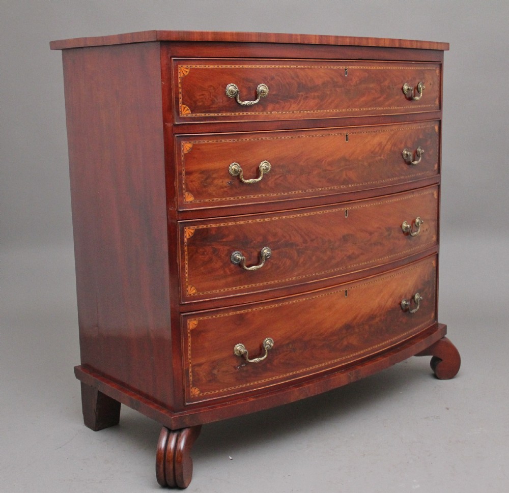 An early nineteenth-century flame mahogany bowfront chest featuring four graduated drawers with inlaid banding and brass handles. View II