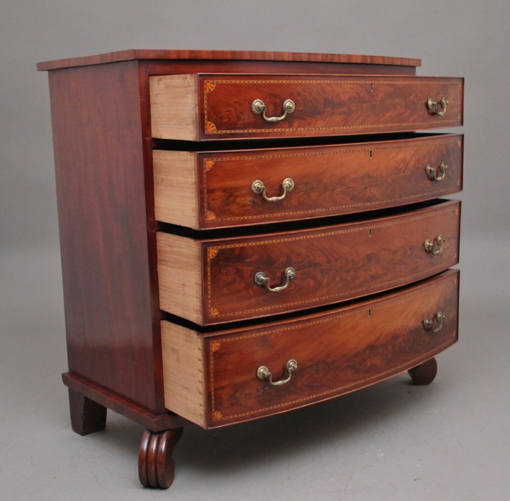 An early nineteenth-century flame mahogany bowfront chest featuring four graduated drawers with inlaid banding and brass handles. View III