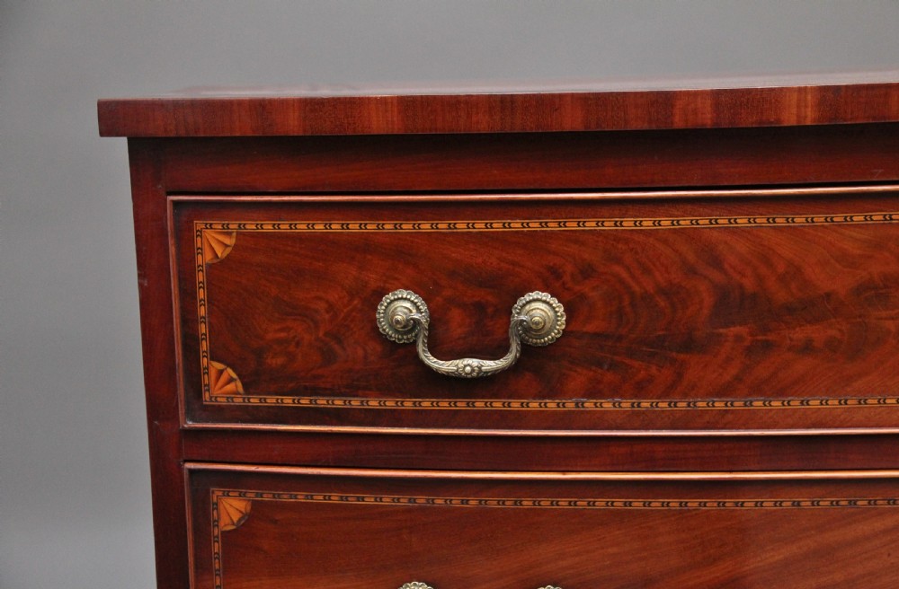 An early nineteenth-century flame mahogany bowfront chest featuring four graduated drawers with inlaid banding and brass handles. View IX
