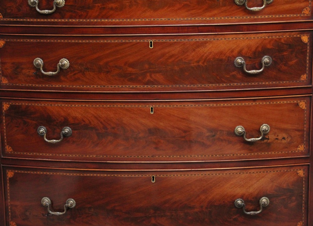 An early nineteenth-century flame mahogany bowfront chest featuring four graduated drawers with inlaid banding and brass handles. View X
