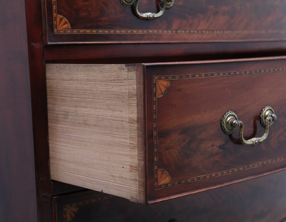 An early nineteenth-century flame mahogany bowfront chest featuring four graduated drawers with inlaid banding and brass handles. View XI