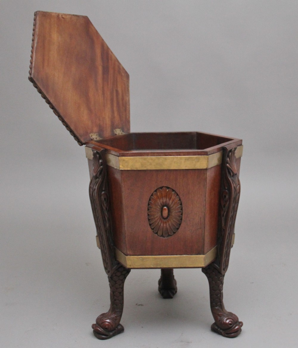 An early twentieth-century mahogany wine cooler featuring a gadrooned hinged lid with turned finial, brass strapping, carved rosette details, and carved dolphin legs. View II