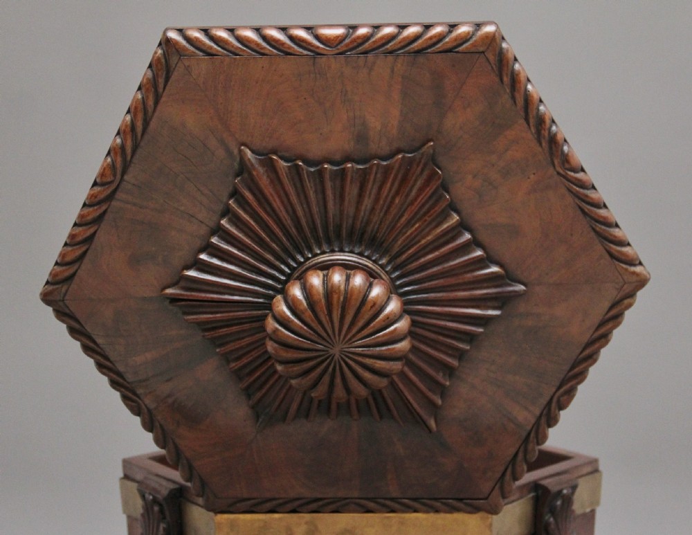 An early twentieth-century mahogany wine cooler featuring a gadrooned hinged lid with turned finial, brass strapping, carved rosette details, and carved dolphin legs. View IX