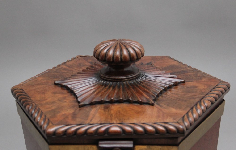 An early twentieth-century mahogany wine cooler featuring a gadrooned hinged lid with turned finial, brass strapping, carved rosette details, and carved dolphin legs. View XI