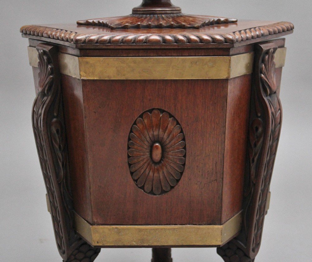 An early twentieth-century mahogany wine cooler featuring a gadrooned hinged lid with turned finial, brass strapping, carved rosette details, and carved dolphin legs. View XII