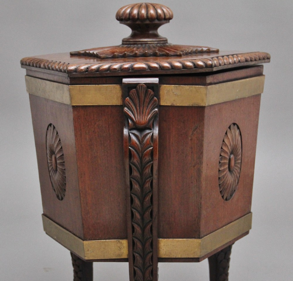 An early twentieth-century mahogany wine cooler featuring a gadrooned hinged lid with turned finial, brass strapping, carved rosette details, and carved dolphin legs. View XIII