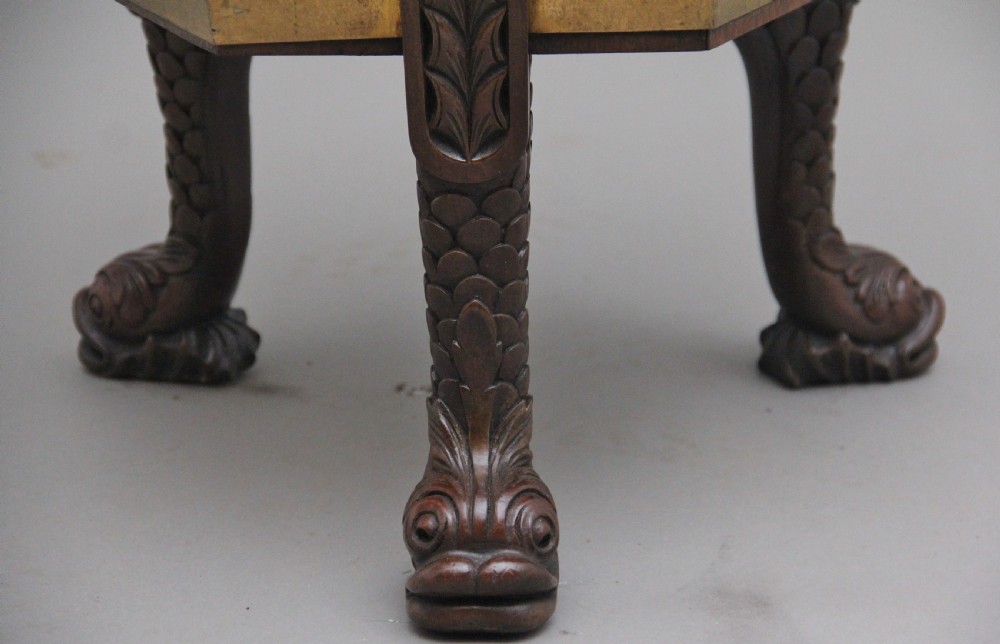 An early twentieth-century mahogany wine cooler featuring a gadrooned hinged lid with turned finial, brass strapping, carved rosette details, and carved dolphin legs. View XIV