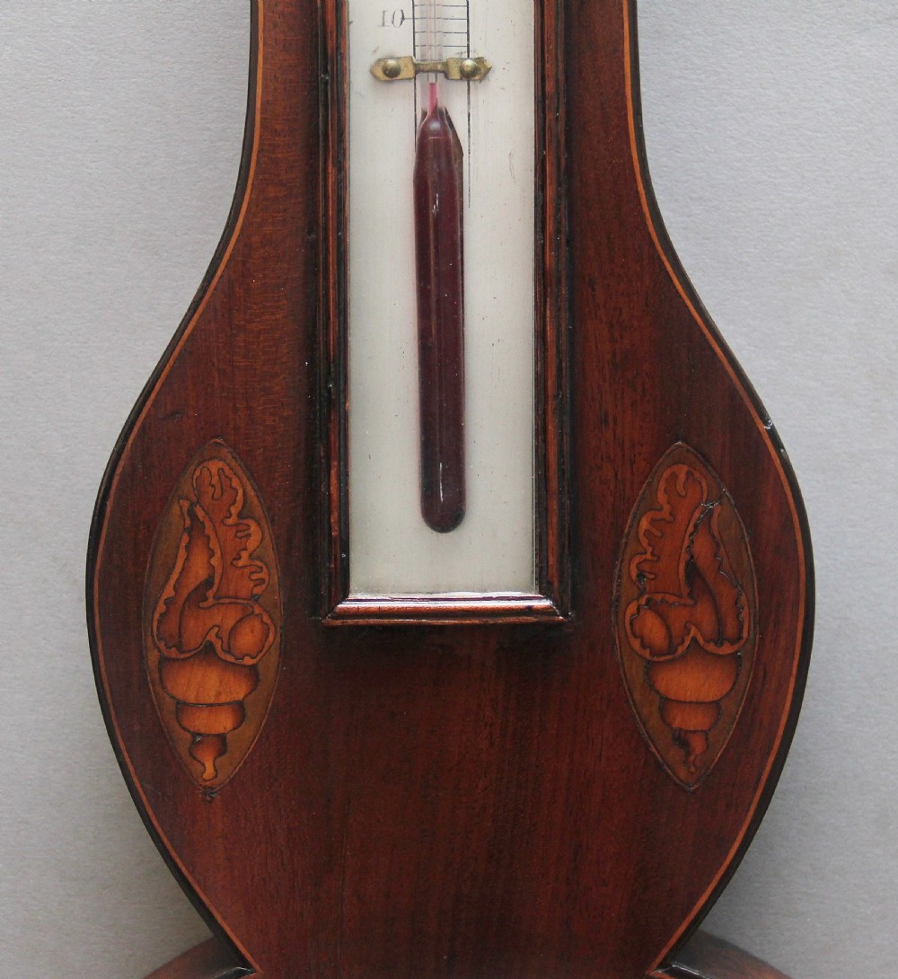 A 19th-century mahogany banjo barometer featuring shell marquetry inlays, a thermometer housing, a broken arch pediment, and a silvered dial. View V