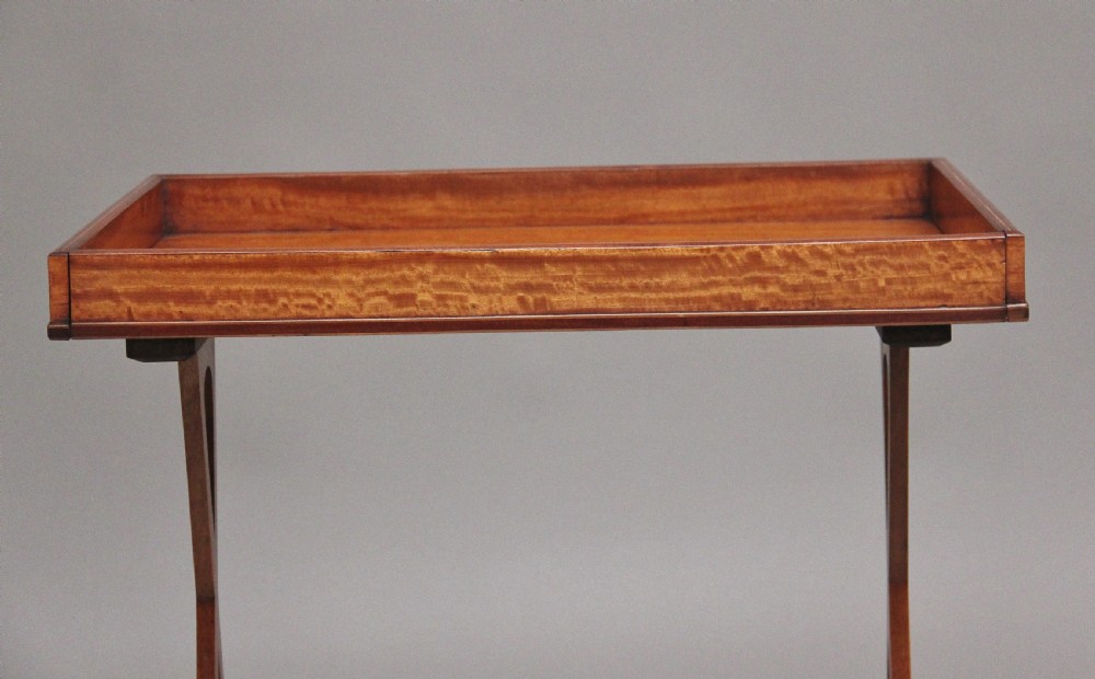 A 19th-century Sheraton Revival satinwood serving table featuring a tray top, pierced side supports, a lower shelf, and splayed legs on brass castors. View V