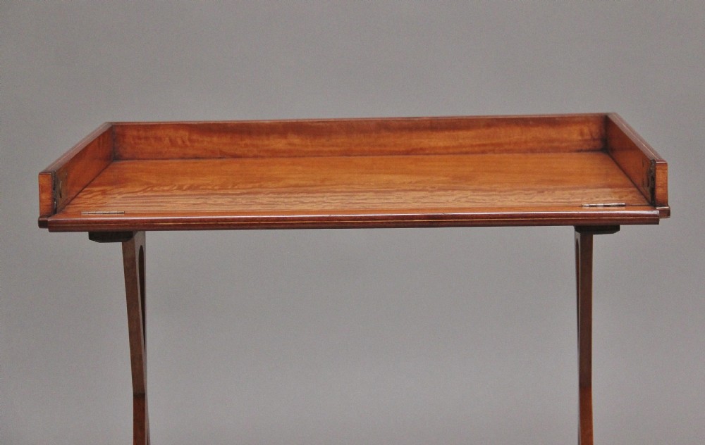 A 19th-century Sheraton Revival satinwood serving table featuring a tray top, pierced side supports, a lower shelf, and splayed legs on brass castors. View VI