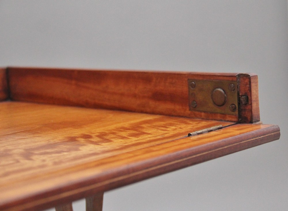 A 19th-century Sheraton Revival satinwood serving table featuring a tray top, pierced side supports, a lower shelf, and splayed legs on brass castors. View VIII