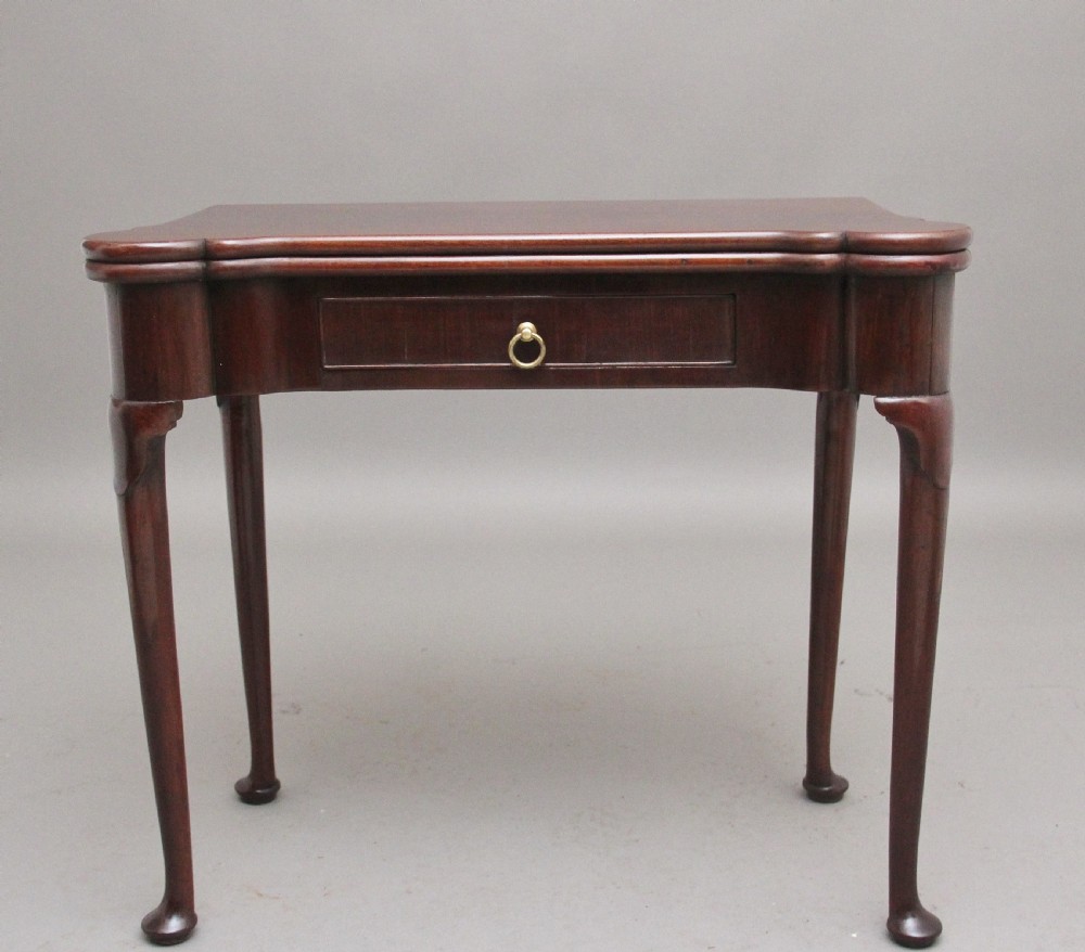 A mid-18th-century mahogany card table featuring a fold-over top, a single frieze drawer with a brass ring handle, and cabriole legs with pad feet.