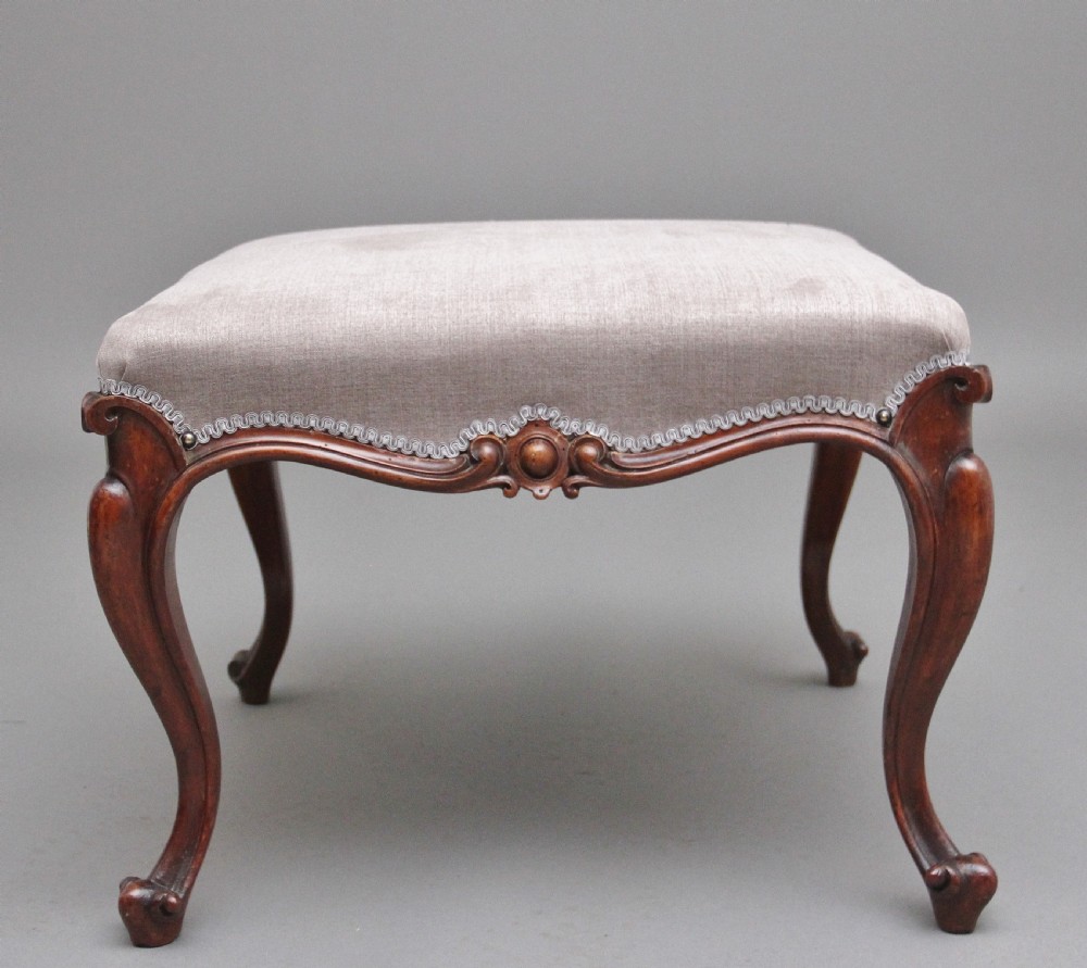 A nineteenth-century Victorian walnut footstool featuring carved cabriole legs, shaped aprons, and light grey fabric upholstery detailed with braided gimp trim. View II