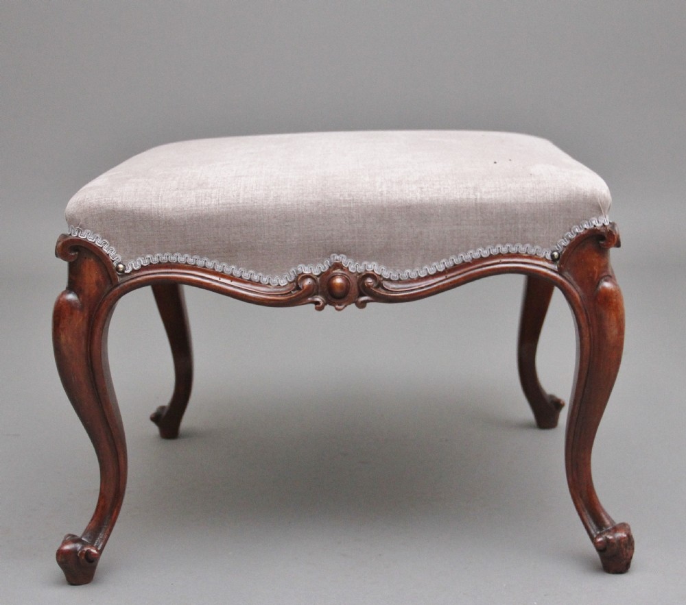 A nineteenth-century Victorian walnut footstool featuring carved cabriole legs, shaped aprons, and light grey fabric upholstery detailed with braided gimp trim. View III