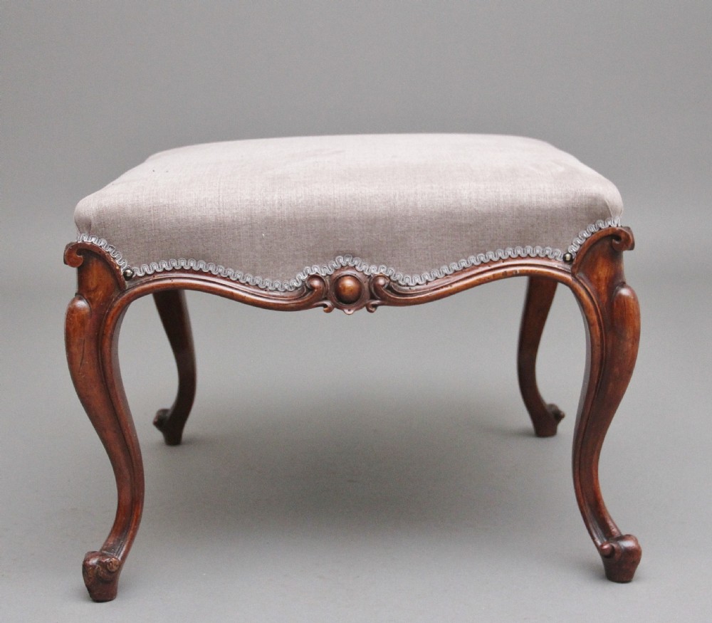 A nineteenth-century Victorian walnut footstool featuring carved cabriole legs, shaped aprons, and light grey fabric upholstery detailed with braided gimp trim. View IV