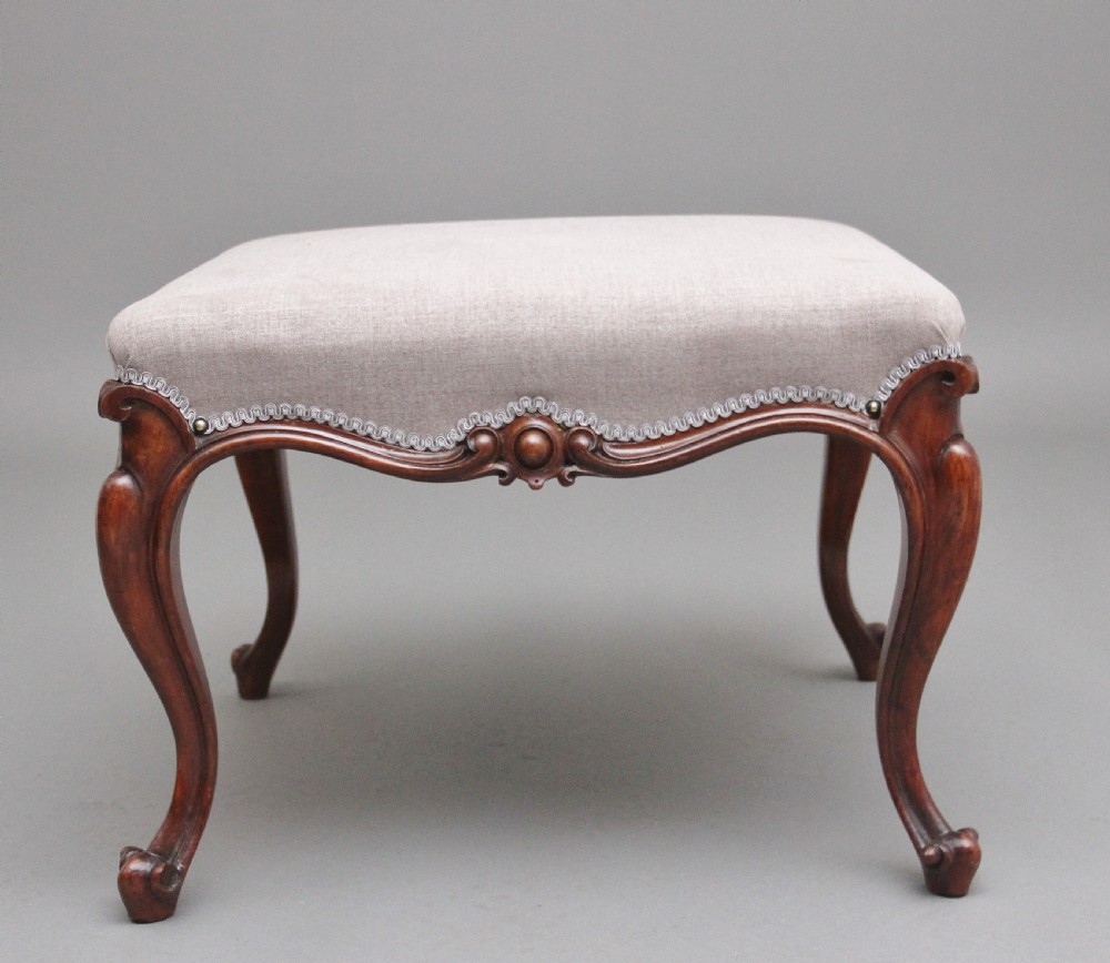 A nineteenth-century Victorian walnut footstool featuring carved cabriole legs, shaped aprons, and light grey fabric upholstery detailed with braided gimp trim. View V