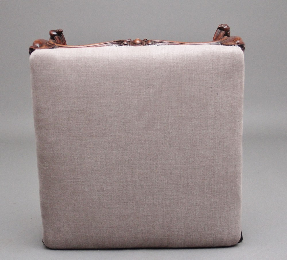 A nineteenth-century Victorian walnut footstool featuring carved cabriole legs, shaped aprons, and light grey fabric upholstery detailed with braided gimp trim. View VI