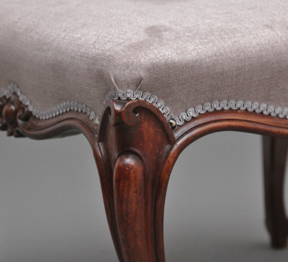 A nineteenth-century Victorian walnut footstool featuring carved cabriole legs, shaped aprons, and light grey fabric upholstery detailed with braided gimp trim. View VII