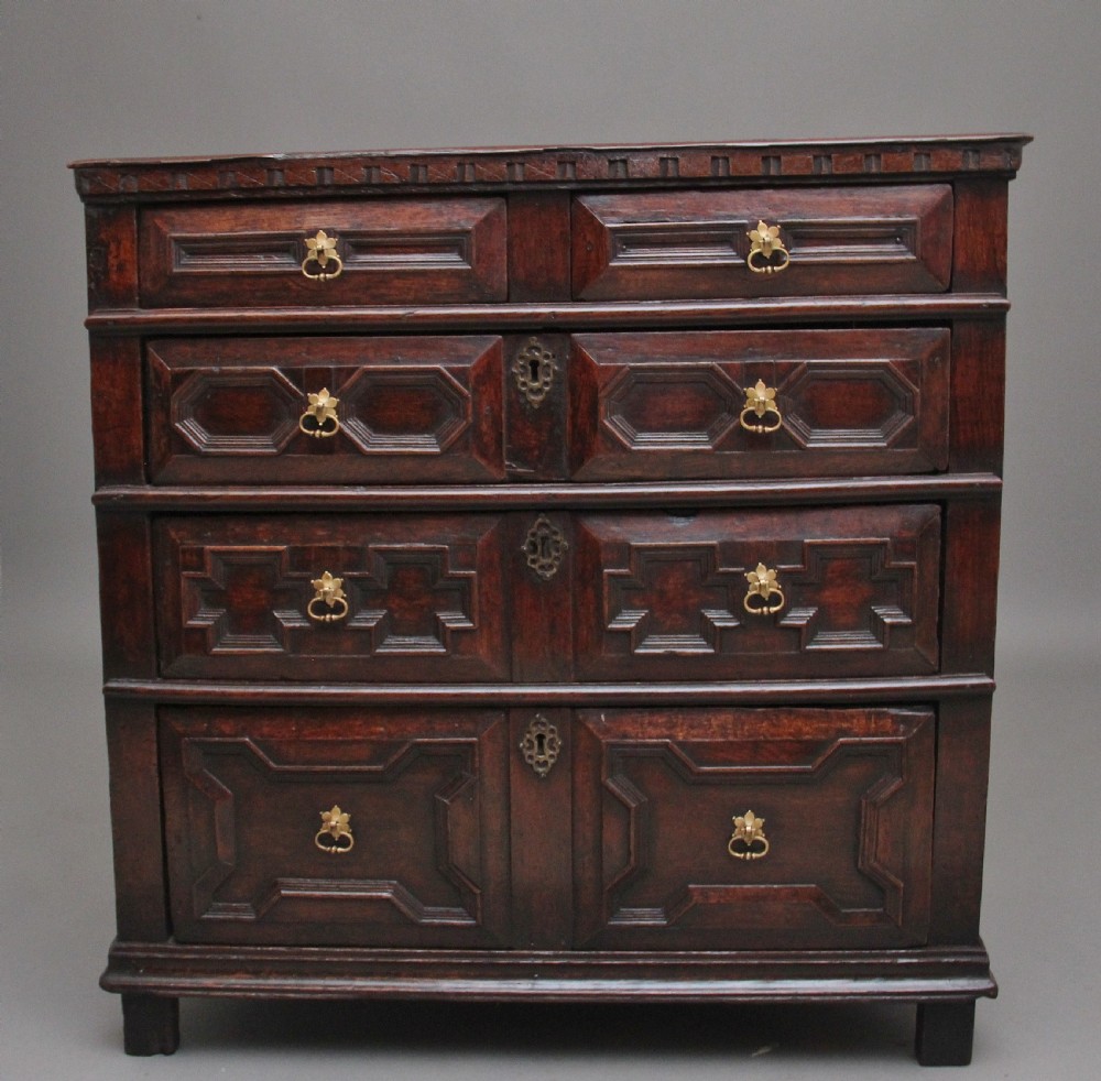 An early eighteenth century dark oak chest of drawers featuring geometric moulded drawer fronts, carved frieze, and brass drop handles.