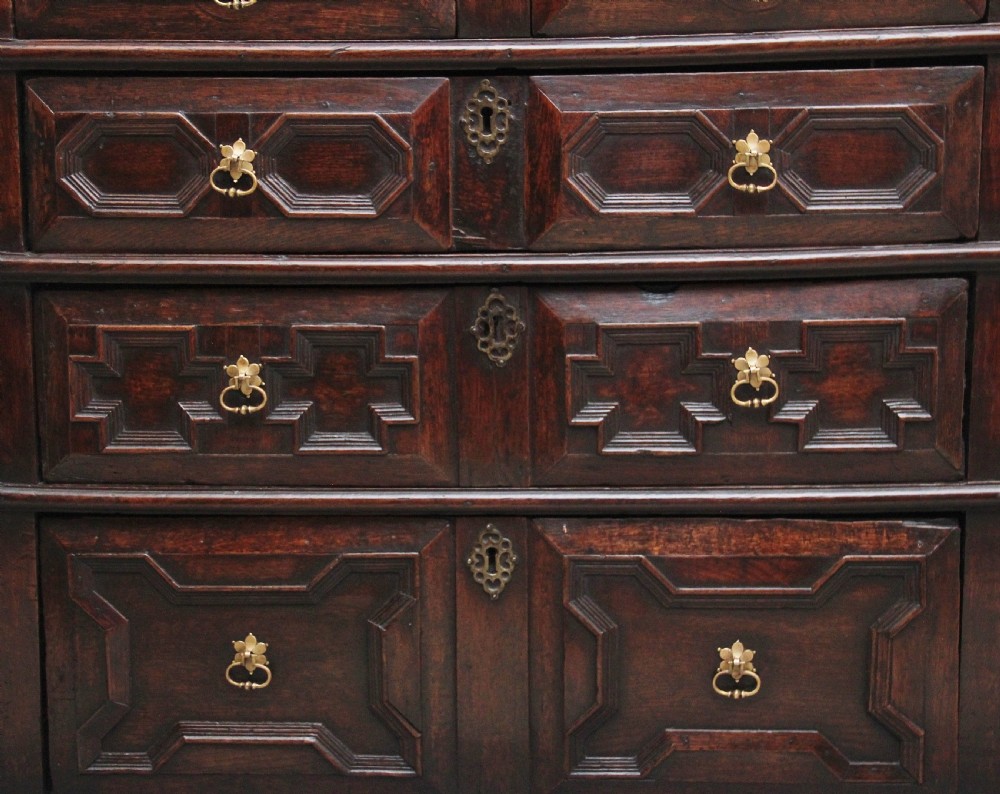 An early eighteenth century dark oak chest of drawers featuring geometric moulded drawer fronts, carved frieze, and brass drop handles. View III