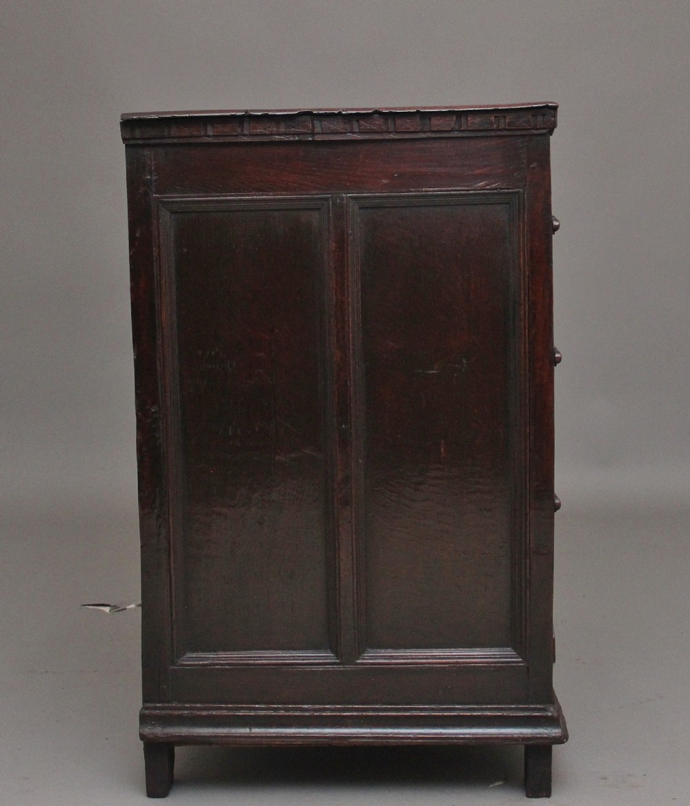 An early eighteenth century dark oak chest of drawers featuring geometric moulded drawer fronts, carved frieze, and brass drop handles. View VII