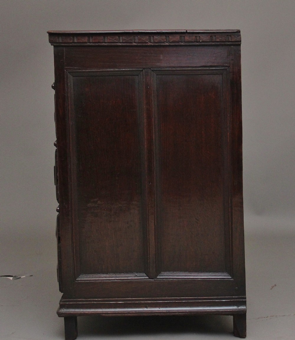 An early eighteenth century dark oak chest of drawers featuring geometric moulded drawer fronts, carved frieze, and brass drop handles. View IX