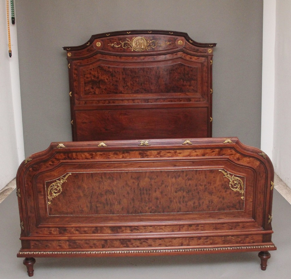 A 19th-century French Neoclassical bed frame crafted from dark mottled mahogany featuring decorative brass scroll mounts and a carved central medallion.