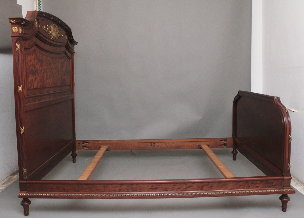 A 19th-century French Neoclassical bed frame crafted from dark mottled mahogany featuring decorative brass scroll mounts and a carved central medallion. View XIII