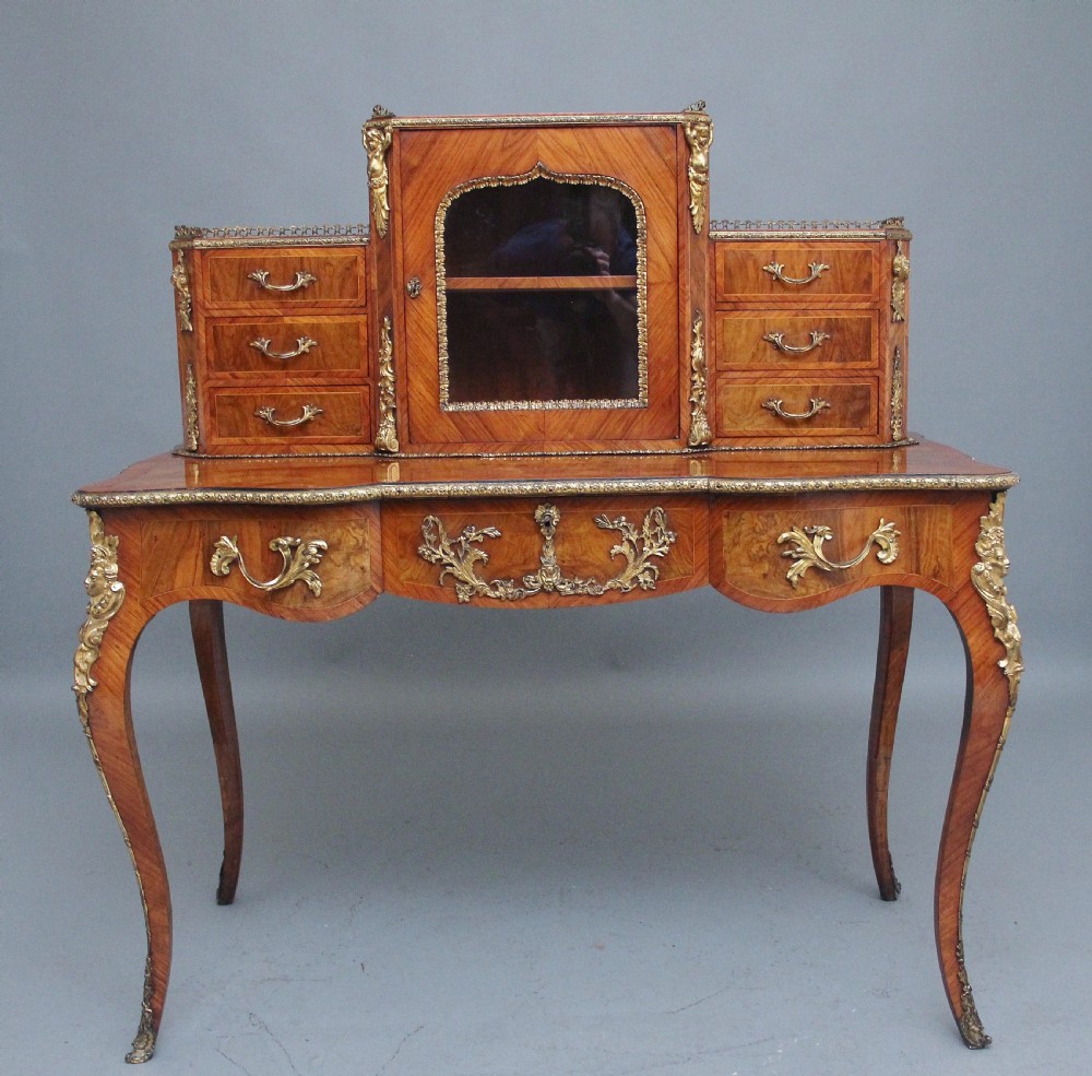 A 19th-century walnut writing desk featuring ornamental gilt-bronze mounts, cabriole legs, and a raised central glazed cabinet flanked by drawers.