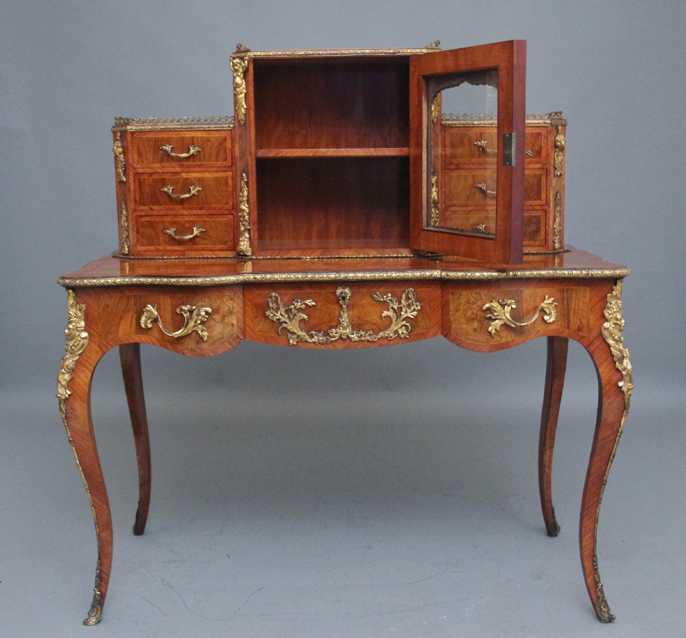 A 19th-century walnut writing desk featuring ornamental gilt-bronze mounts, cabriole legs, and a raised central glazed cabinet flanked by drawers. View IV