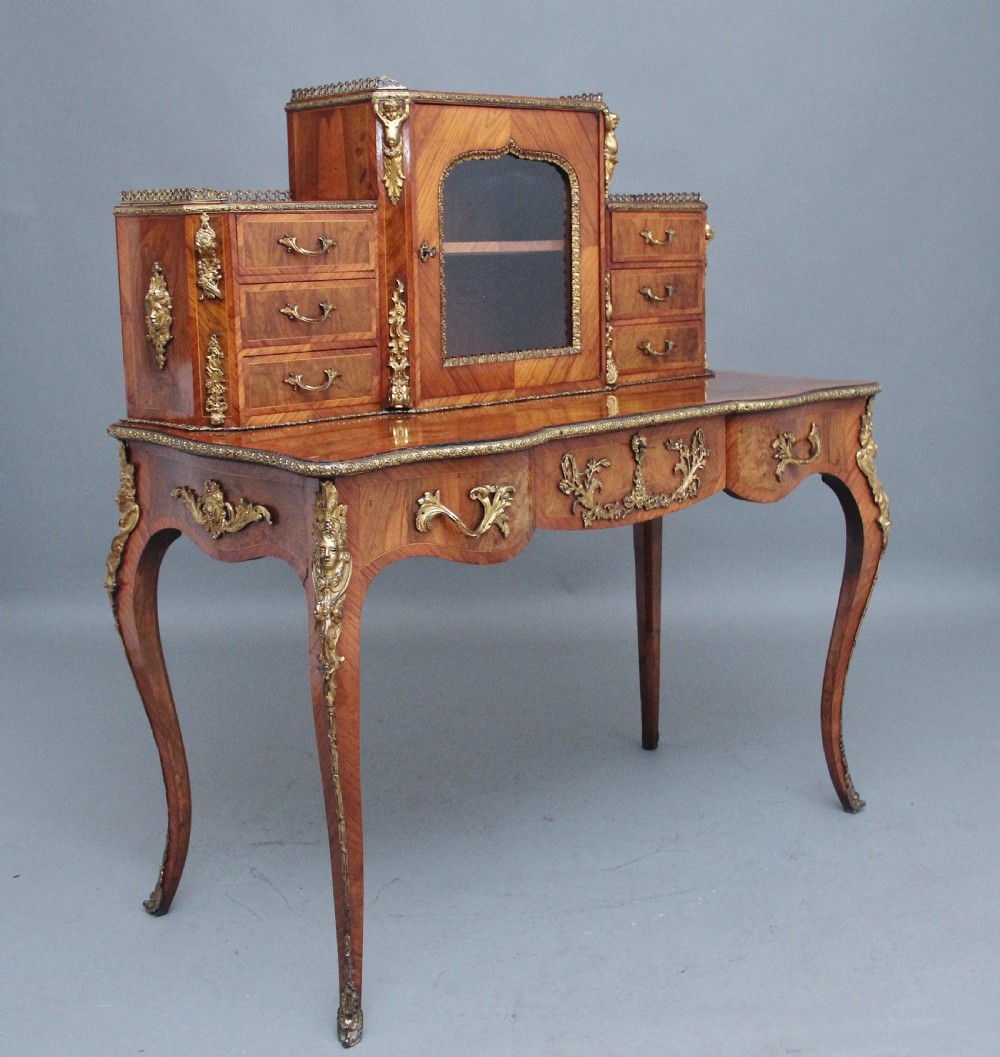 A 19th-century walnut writing desk featuring ornamental gilt-bronze mounts, cabriole legs, and a raised central glazed cabinet flanked by drawers. View V