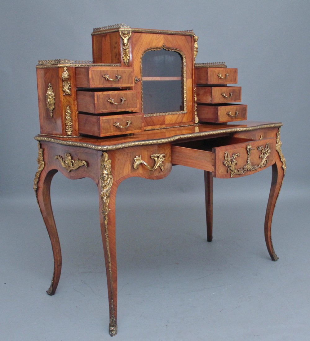 A 19th-century walnut writing desk featuring ornamental gilt-bronze mounts, cabriole legs, and a raised central glazed cabinet flanked by drawers. View VI