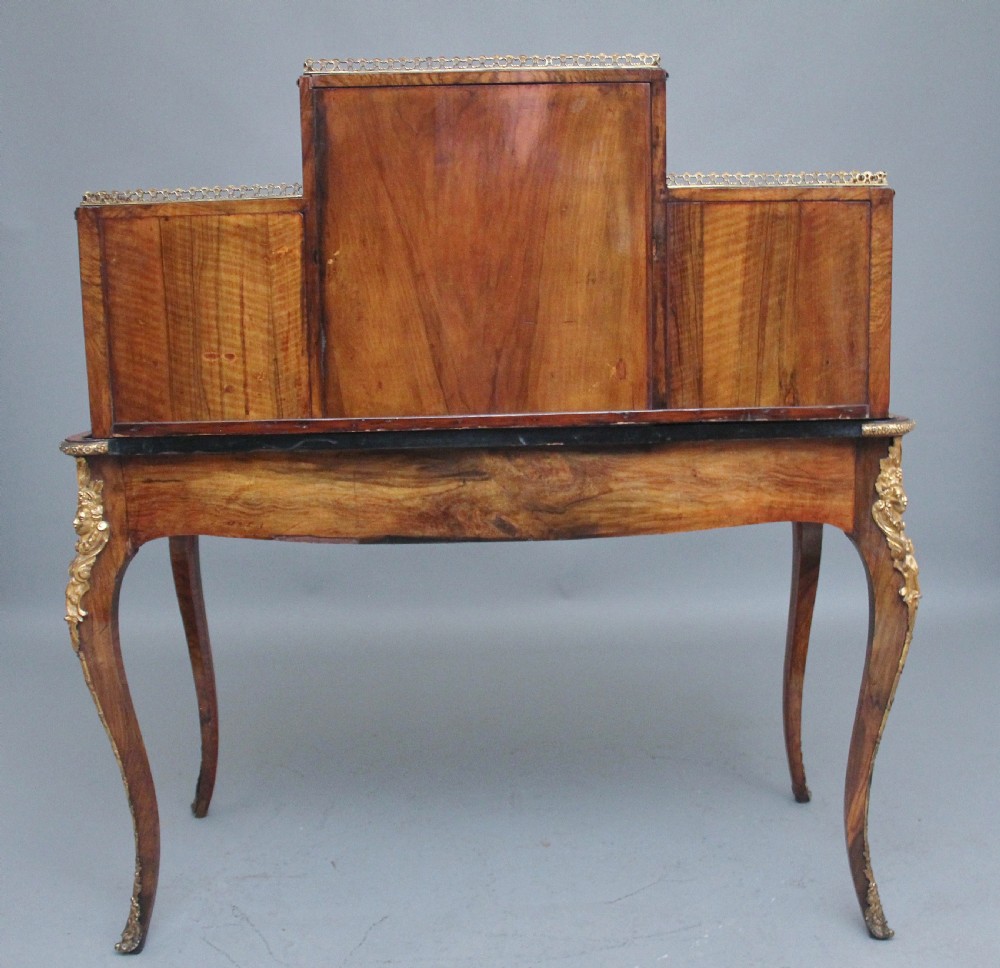 A 19th-century walnut writing desk featuring ornamental gilt-bronze mounts, cabriole legs, and a raised central glazed cabinet flanked by drawers. View X