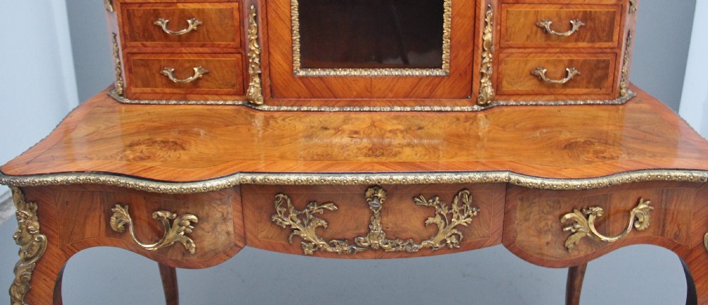 A 19th-century walnut writing desk featuring ornamental gilt-bronze mounts, cabriole legs, and a raised central glazed cabinet flanked by drawers. View XV