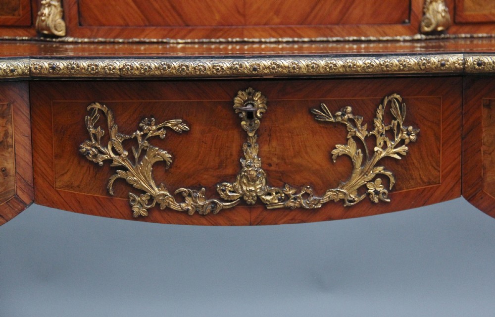A 19th-century walnut writing desk featuring ornamental gilt-bronze mounts, cabriole legs, and a raised central glazed cabinet flanked by drawers. View XXII