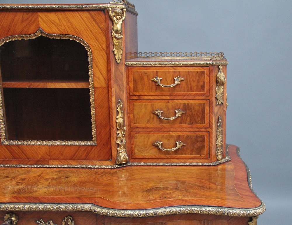 A 19th-century walnut writing desk featuring ornamental gilt-bronze mounts, cabriole legs, and a raised central glazed cabinet flanked by drawers. View XXIV