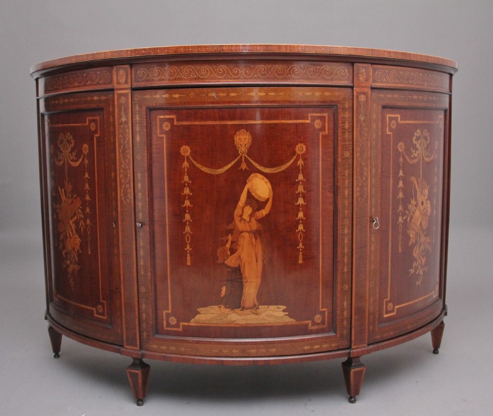A 19th-century curved mahogany cabinet featuring intricate satinwood marquetry panels depicting classical figures, swags, and scrollwork.