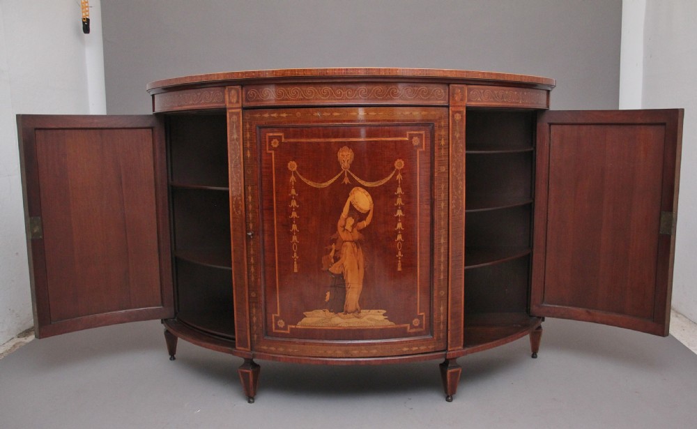 A 19th-century curved mahogany cabinet featuring intricate satinwood marquetry panels depicting classical figures, swags, and scrollwork. View III