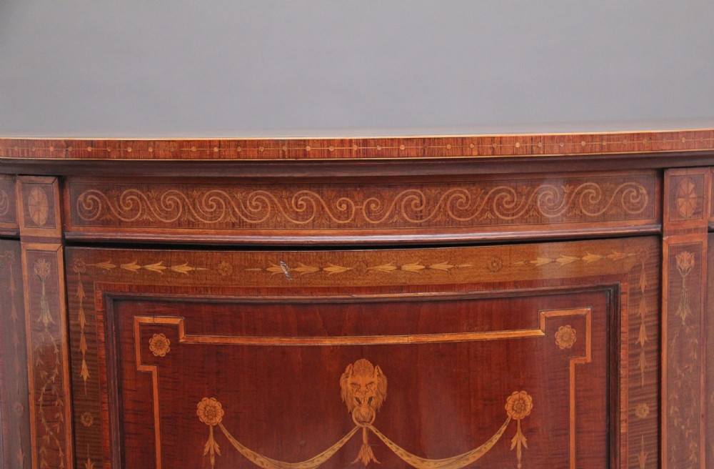 A 19th-century curved mahogany cabinet featuring intricate satinwood marquetry panels depicting classical figures, swags, and scrollwork. View IX
