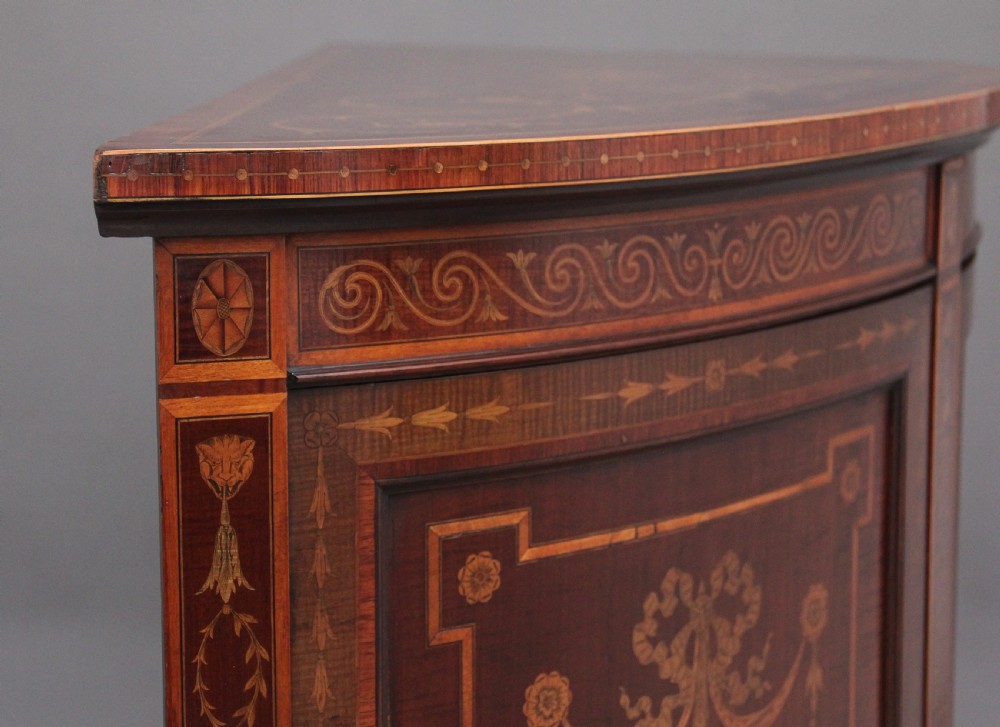 A 19th-century curved mahogany cabinet featuring intricate satinwood marquetry panels depicting classical figures, swags, and scrollwork. View X