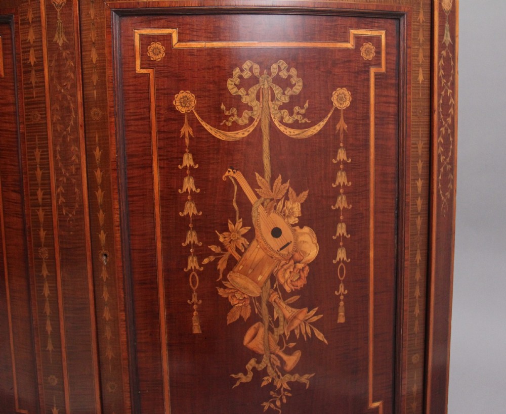 A 19th-century curved mahogany cabinet featuring intricate satinwood marquetry panels depicting classical figures, swags, and scrollwork. View XIV