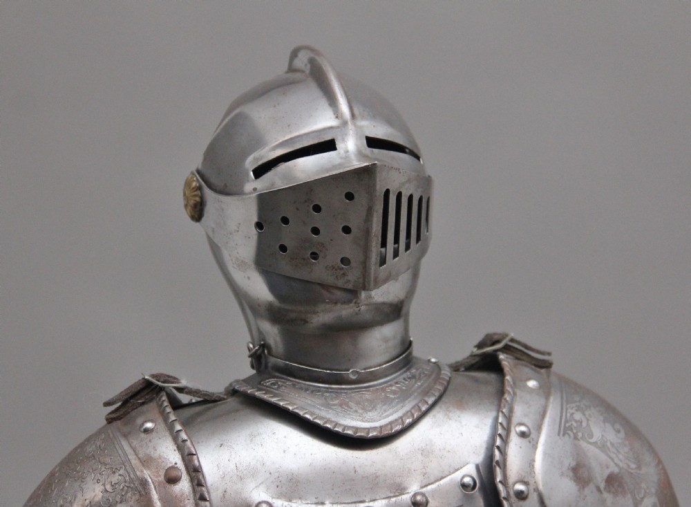 A detailed miniature suit of polished steel plate armour with fine surface etchings, brass eagle emblems, and red fabric lining, standing on a dark wood base. View VI