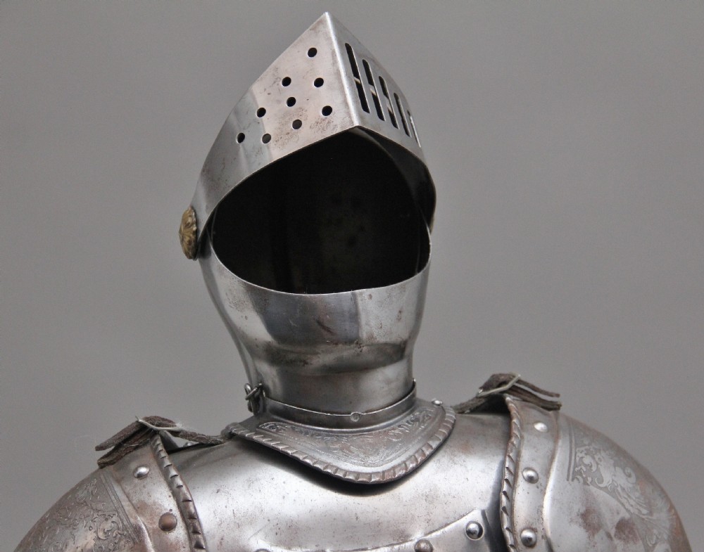 A detailed miniature suit of polished steel plate armour with fine surface etchings, brass eagle emblems, and red fabric lining, standing on a dark wood base. View VII