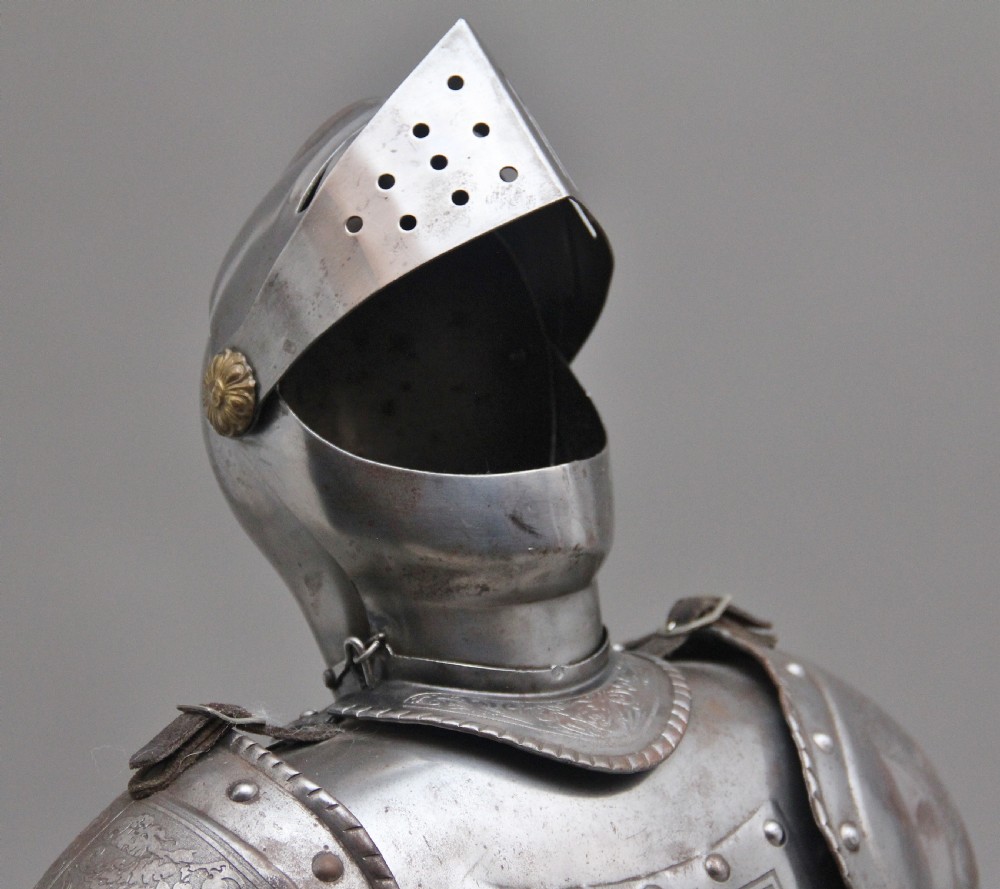 A detailed miniature suit of polished steel plate armour with fine surface etchings, brass eagle emblems, and red fabric lining, standing on a dark wood base. View VIII