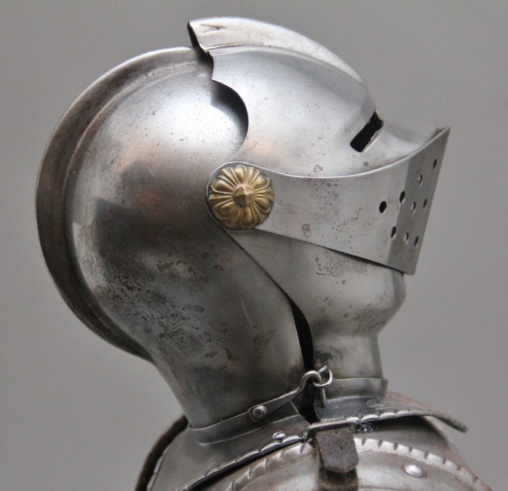 A detailed miniature suit of polished steel plate armour with fine surface etchings, brass eagle emblems, and red fabric lining, standing on a dark wood base. View X