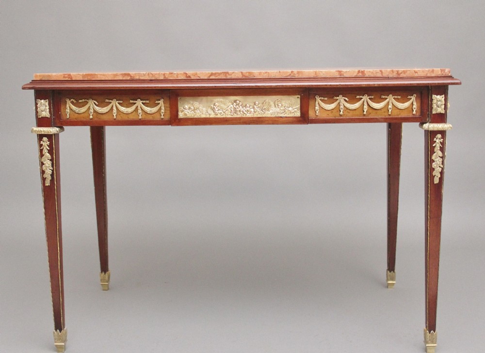A 19th-century French mahogany centre table featuring a pink marble top, slender tapered legs, and decorative gilt-bronze mounts with swags and cherub relief.