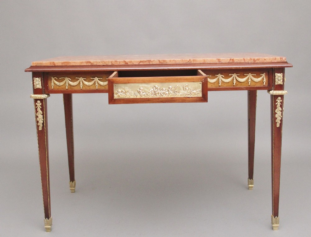 A 19th-century French mahogany centre table featuring a pink marble top, slender tapered legs, and decorative gilt-bronze mounts with swags and cherub relief. View II