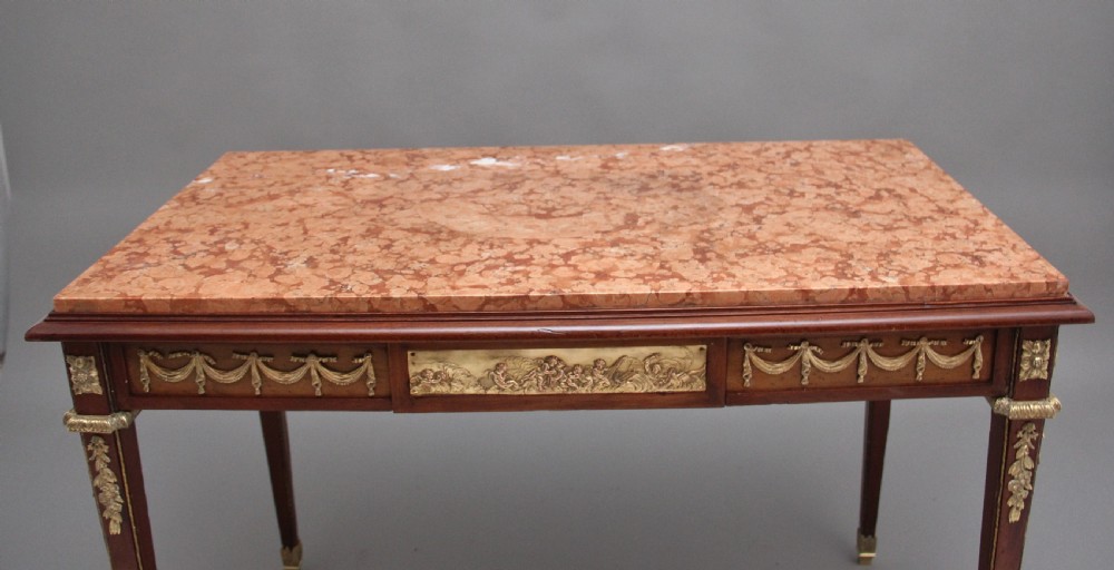 A 19th-century French mahogany centre table featuring a pink marble top, slender tapered legs, and decorative gilt-bronze mounts with swags and cherub relief. View III