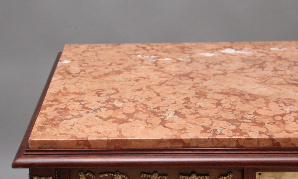 A 19th-century French mahogany centre table featuring a pink marble top, slender tapered legs, and decorative gilt-bronze mounts with swags and cherub relief. View IV