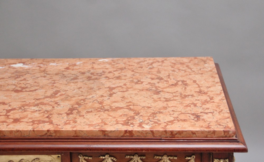 A 19th-century French mahogany centre table featuring a pink marble top, slender tapered legs, and decorative gilt-bronze mounts with swags and cherub relief. View V